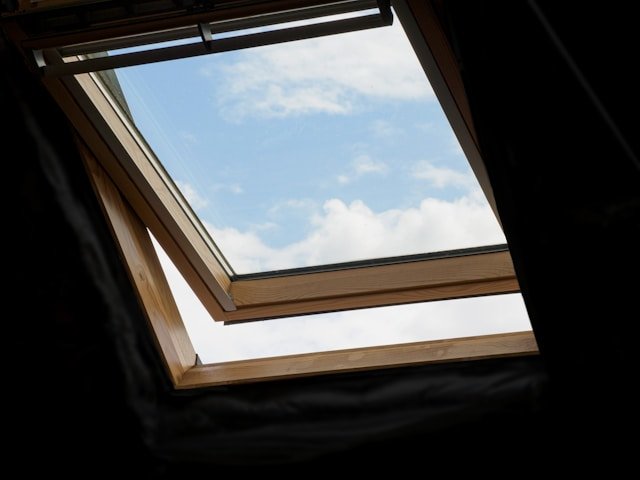 Roof window installation allowing natural light and ventilation, with a view of the sky and soft clouds visible through the open window.