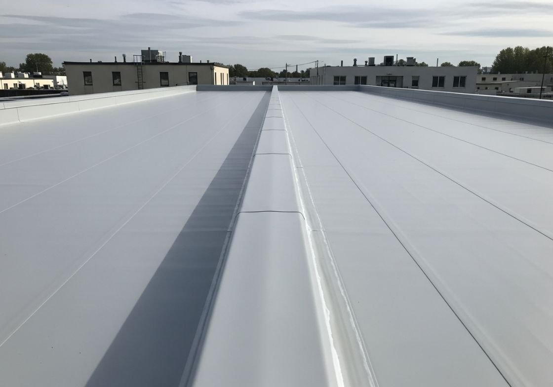A clean white TPO roofing system with a central drainage line and neatly aligned seams on a flat commercial roof.